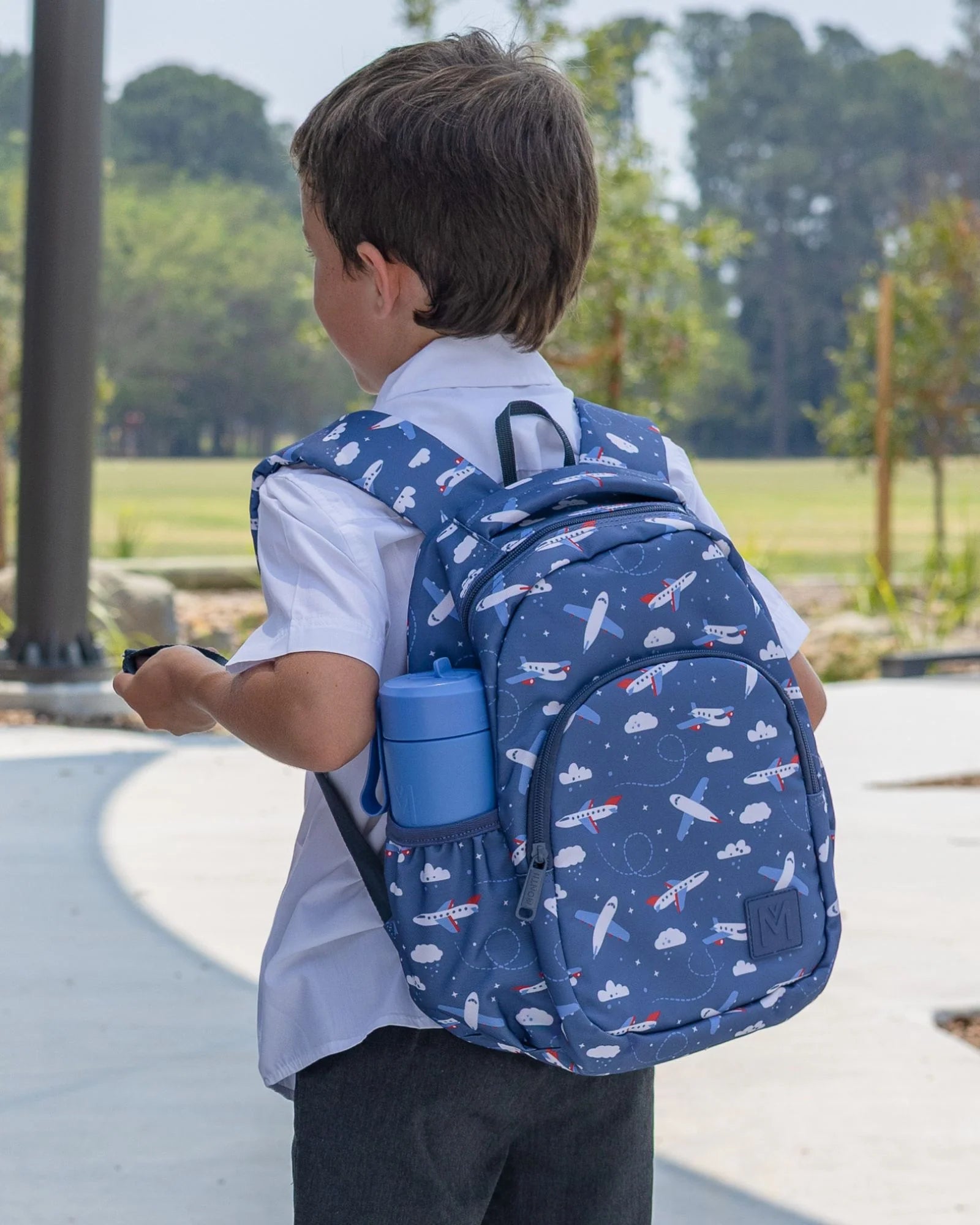 Child wearing a blue backpack with airplane pattern outdoors