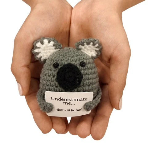 hands holding a handmade crochet koala plush toy with a cheeky “Underestimate me… that will be fun!” sign