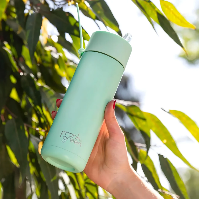 Mint Frank Green bottle with flip straw lid held outdoors in leafy sunshine — Adventure Awaits