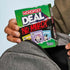 Adventure Awaits Monopoly Deal No Mercy card game pack held above a backpack pocket for travel play