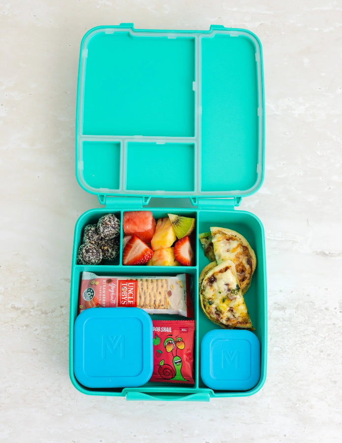 Open teal Montii bento lunchbox packed with fruit, snacks, quiche and blue snack containers — Adventure Awaits