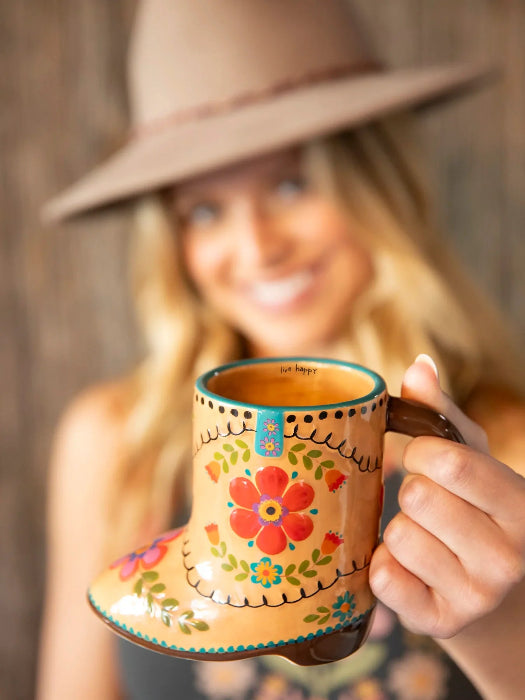 Woman holding a colourful cowboy boot shaped ceramic mug with floral artwork and “live happy” message