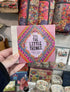 Hand holding It’s the Little Things happy notes booklet in colourful gift shop display — Adventure Awaits