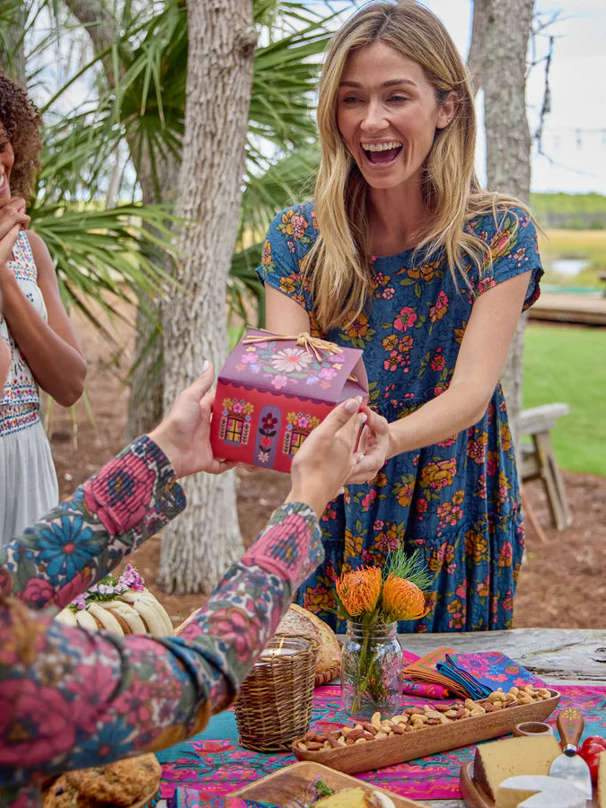 Smiling woman receiving floral cottage gift box at outdoor picnic table, unique gift packaging for special occasions Adventure Awaits