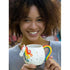 Smiling woman holding a unicorn shaped ceramic mug with rainbow handle and inspirational quote design
