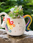 Unicorn shaped ceramic planter with rainbow mane and tail holding a succulent plant outdoors