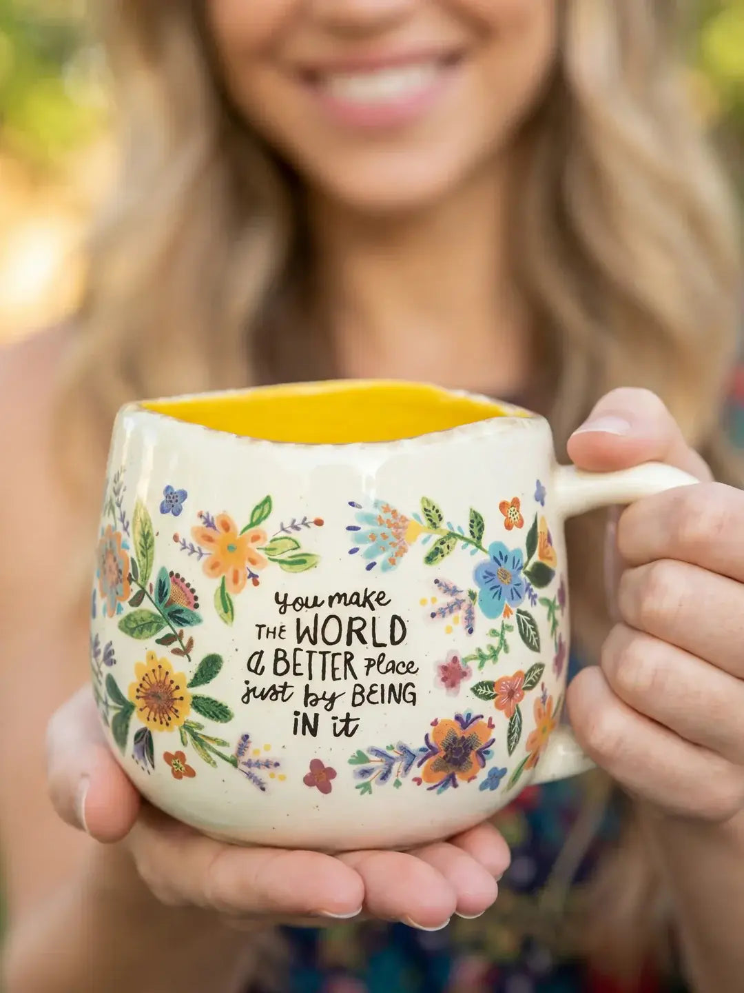 Woman holding Natural Life floral mug with yellow interior and uplifting “better place” quote — Adventure Awaits