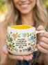 Woman holding Natural Life floral mug with yellow interior and uplifting “better place” quote — Adventure Awaits