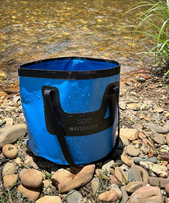 Blue Navigator Folding Bucket Buddy on a rocky creek bank, wet and ready for campsite use - Adventure Awaits
