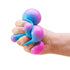 Hand squeezing a pink and blue NeeDoh colour-change sensory cube as soft bubbles bulge out, Adventure Awaits