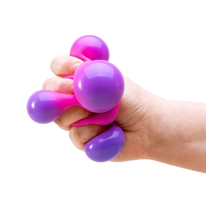 Hand squeezing a pink and purple NeeDoh colour-change sensory cube as soft bubbles bulge out, Adventure Awaits