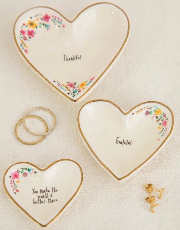 Three heart-shaped ceramic dishes with floral designs and text on a beige background