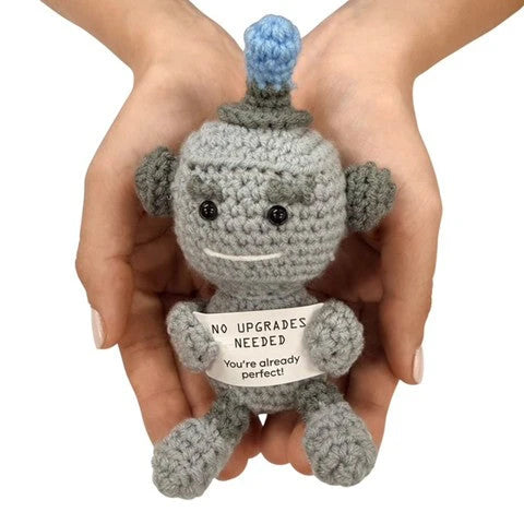 hands holding a handmade crochet robot plush toy with a positive “No upgrades needed” quote sign