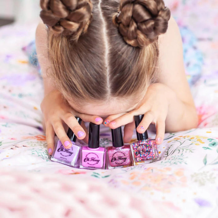 Alt text: Girl with braided hair playing with Oh Flossy kids nail polish bottles, colourful non toxic dress up fun Adventure Awaits