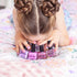 Alt text: Girl with braided hair playing with Oh Flossy kids nail polish bottles, colourful non toxic dress up fun Adventure Awaits