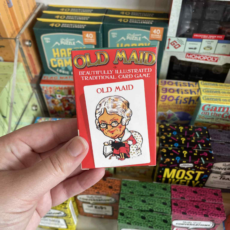 Hand holding a 'Old Maid' card game box with other board games in the background.