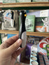 Hand holding a black and gray tool against a store shelf with various items