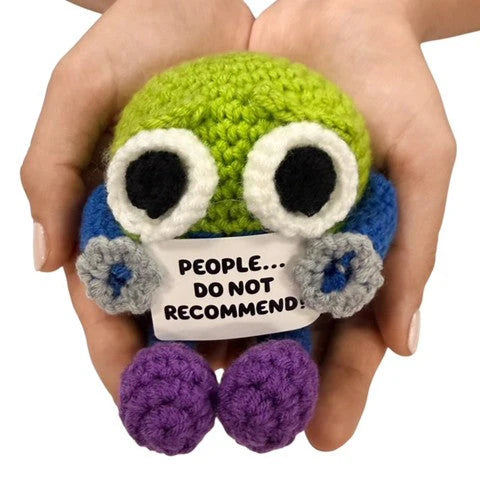 hands holding a quirky handmade crochet plush toy with a funny “People… Do Not Recommend!” sign