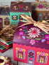 woman unpacking little cottage gift boxes, baking and packing baked goods into assembled boxes then delivering to another woman