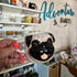 Pug-shaped coffee mug held by a hand with neon orange nail polish, blurred background with 'Adventure Awaits' text.