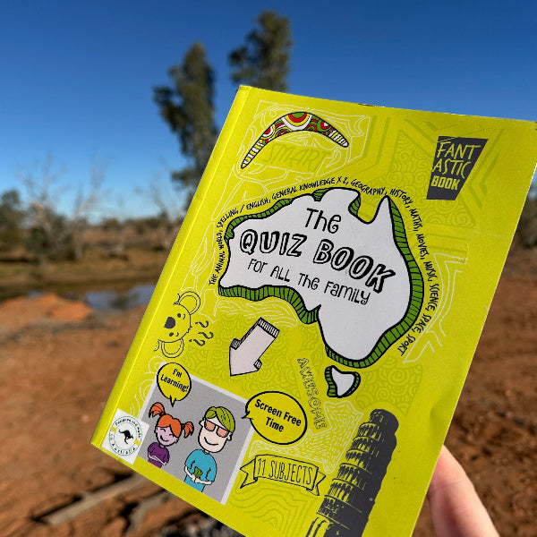 Yellow book titled 'The Ouiz Book' held by a hand with a blurred natural background