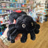Black plush red back spider toy held in a hand with a store in the background