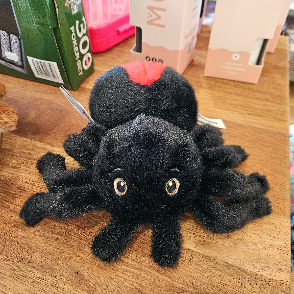 Red Back Black spider plush toy on a wooden surface with a box and books in the background