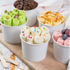 Colorful ice cream cones in white cups on a wooden board with a light background