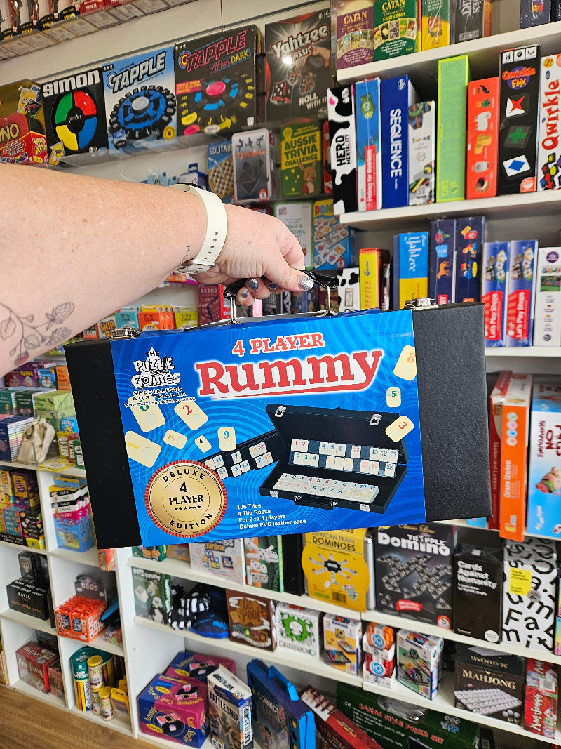 Hand holding a 'Player Rummy' board game box in a store with various games on shelves.