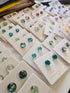 Display of gemstone earrings on white cards with visible brand name.