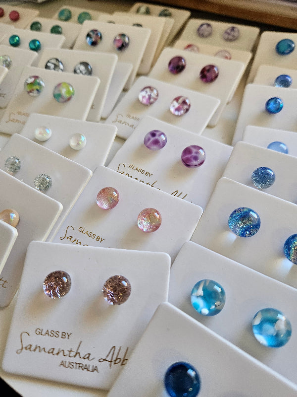 Collection of gemstone earrings on display cards with 'Glass by Samantha Alper' branding.