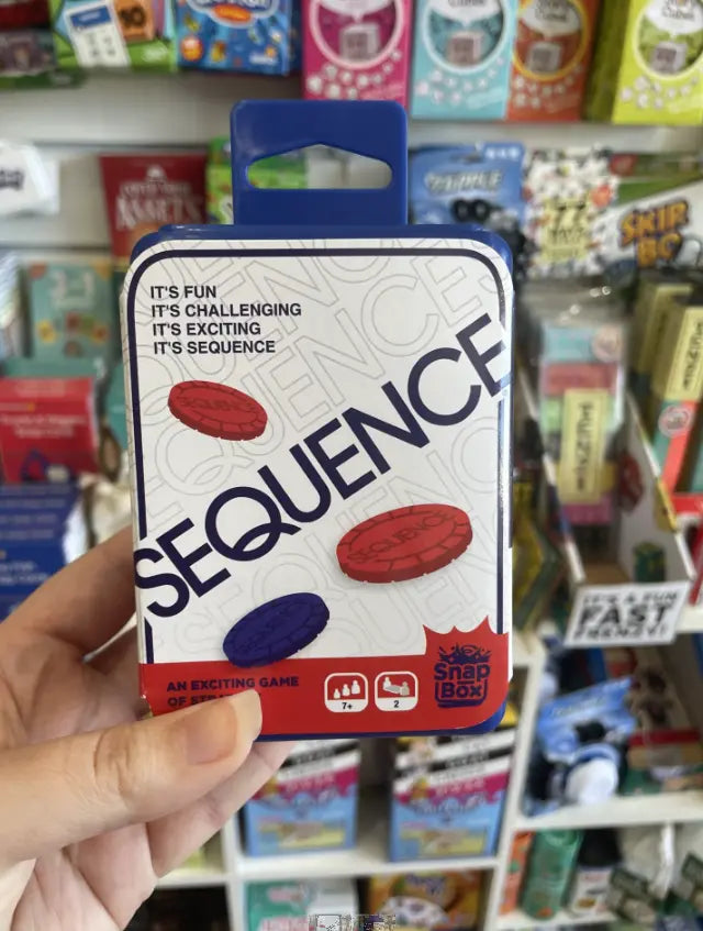 Hand holding compact Sequence strategy game in Snap Box packaging in a shop — Adventure Awaits