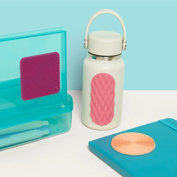White water bottle with speks slabs pink textured grip, turquoise case, and blue notebook on a light blue background