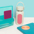 White water bottle with speks slabs pink textured grip, turquoise case, and blue notebook on a light blue background