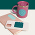 Pink mug with teal lid on a white surface, next to a phone case with teal silicone fidget sticker by speks