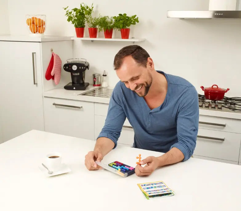 Adult playing Smart Games IQ Fit logic game at kitchen table with challenge cards — Adventure Awaits