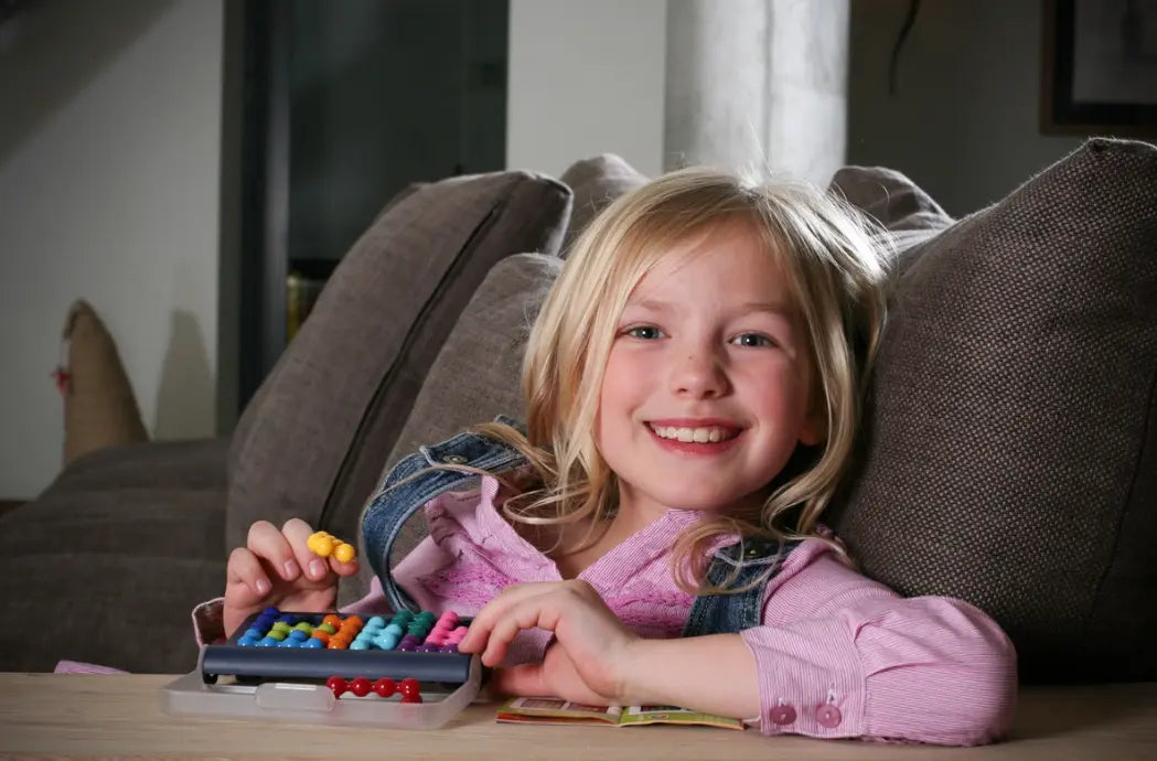 Child playing Smart Games IQ Fit logic game on the couch with colourful pieces — Adventure Awaits