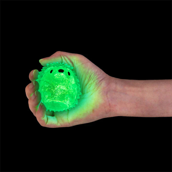 Hand holding a glowing green echidna squishy sensory toy against a black background