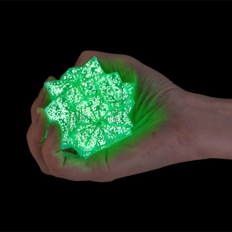 Hand squeezing green glow in the dark starburst squishy toy against black background — Adventure Awaits
