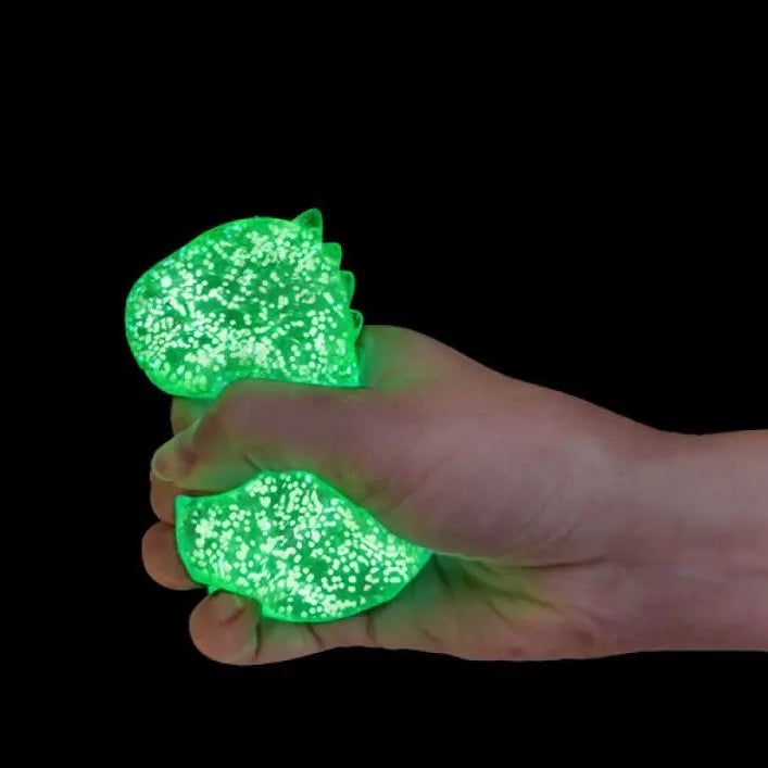 Hand squeezing green glow in the dark dino squishy toy against black background — Adventure Awaits