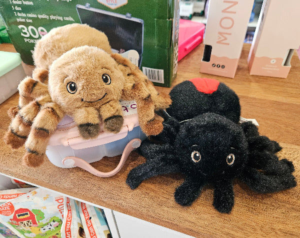 Two plush spider toys on a wooden surface with a box in the background.