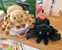 Two plush spider toys on a wooden surface with a box in the background.