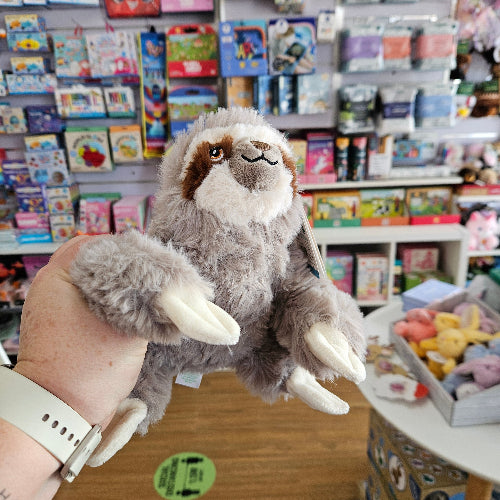 Plush toy resembling a creature with large white tusks held by a person in a store setting.