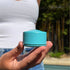 Hand holding blue refillable travel pot outdoors, compact container ideal for storing toiletries and creams for organised packing at home or travel Adventure Awaits