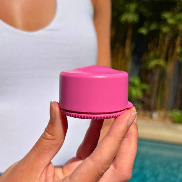 Hand holding pink refillable travel pot outdoors, compact container ideal for storing toiletries and creams for organised packing at home or travel Adventure Awaits