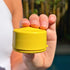 Hand holding yellow refillable travel pot outdoors, compact container ideal for storing toiletries and creams for organised packing at home or travel Adventure Awaits