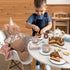 Child playing tea party with wooden cake, teapot and cups at a small table — Adventure Awaits