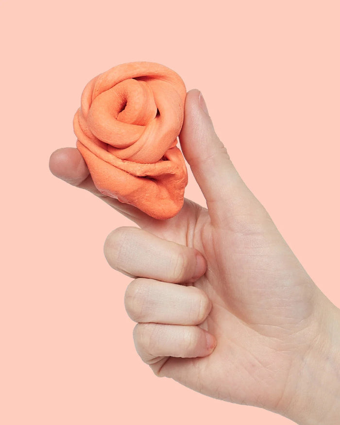 Hand holding soft orange sensory putty twisted into a swirl against a peach background — Adventure Awaits