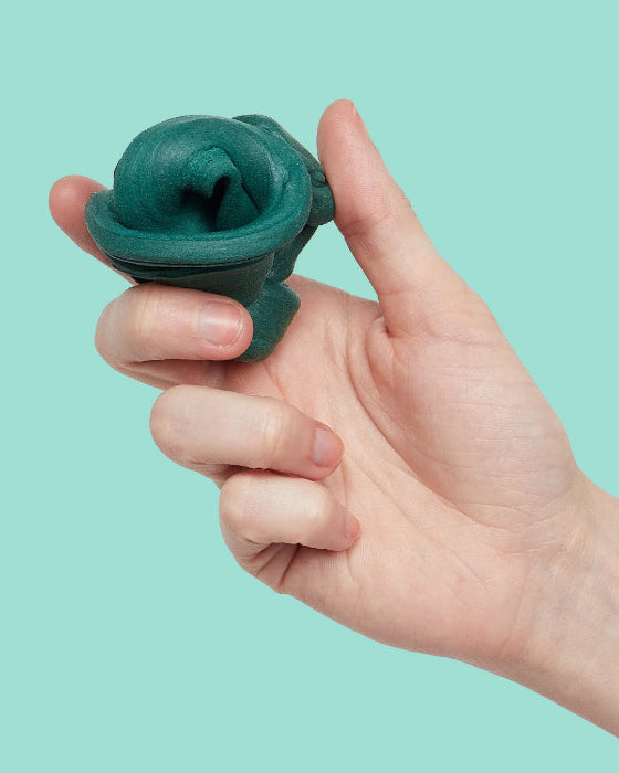 Hand holding dark teal SPEKS Blur calming focus putty against a mint background — Adventure Awaits