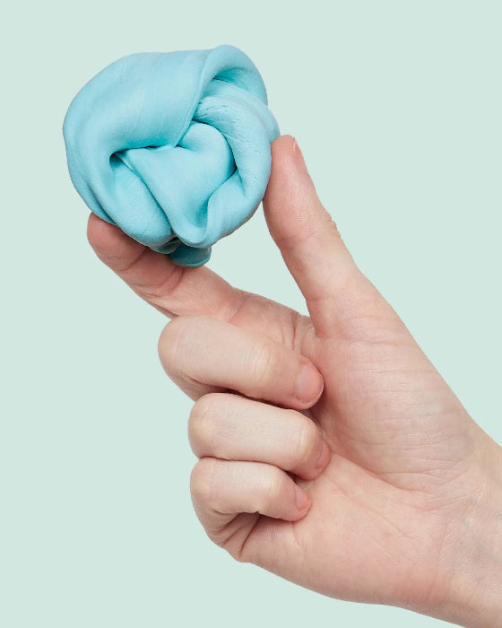 Hand holding soft blue SPEKS Blur calming focus putty against a pale blue background — Adventure Awaits